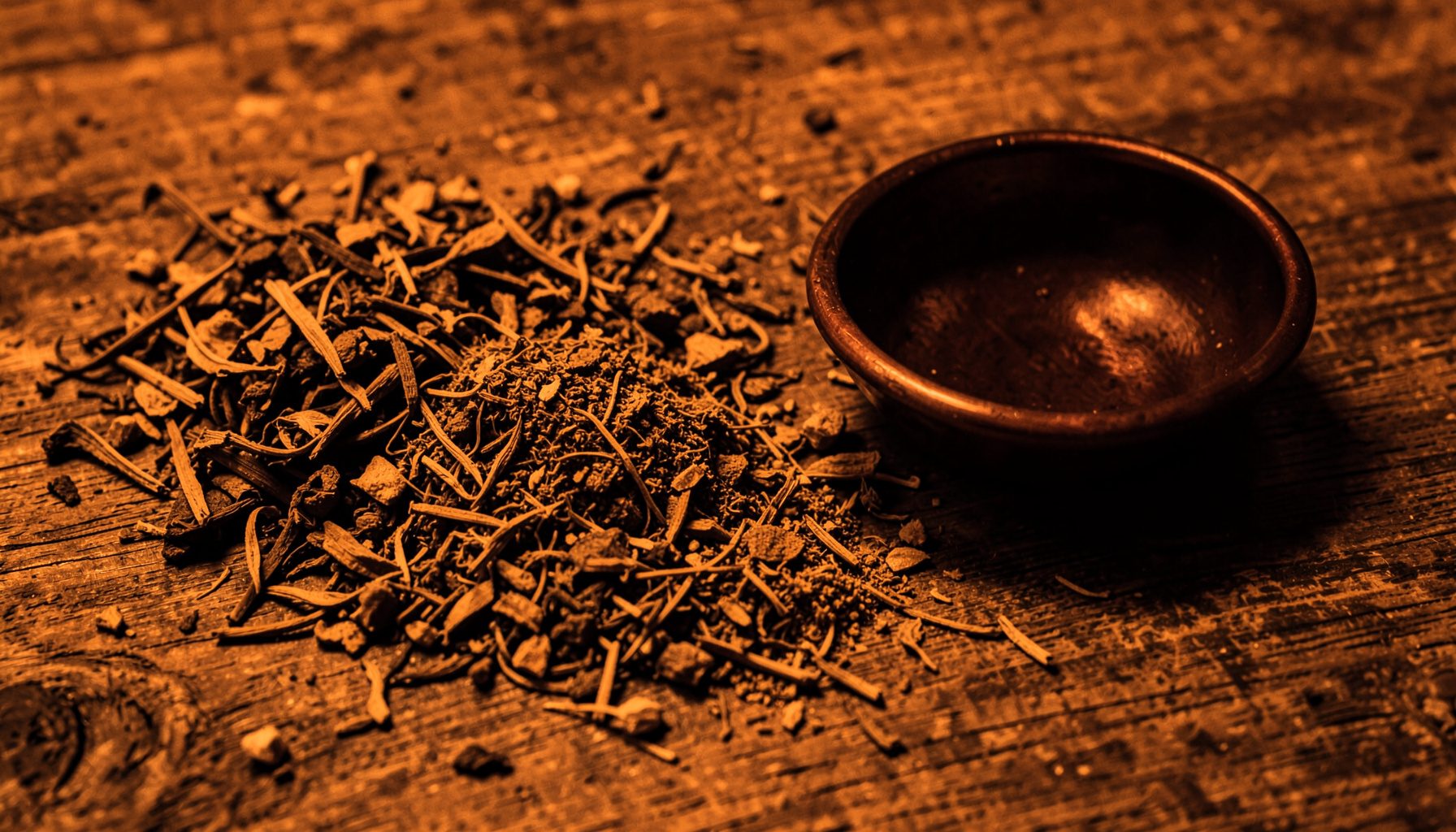 A warm duotone photograph of dried herbs, spices, and a small copper bowl arranged on a textured wooden surface, evoking earthy amber and deep brown tones.